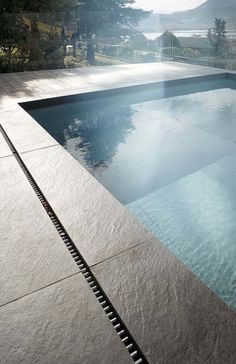 an empty swimming pool in the middle of a patio with trees and mountains in the background