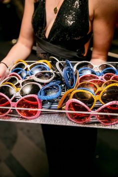 a woman is holding a tray full of sunglasses