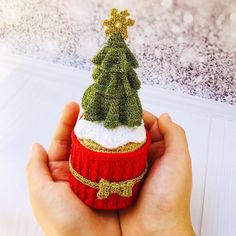 a hand holding a small christmas tree on top of a red cup with gold trim