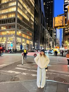 a woman standing in the middle of a city street at night with traffic lights and tall buildings behind her