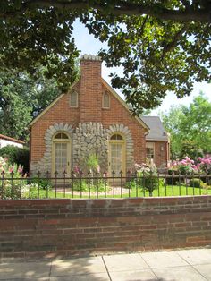 a brick house with a fence surrounding it and flowers in the front yard, on a sunny day