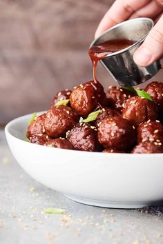 someone pouring sauce on some meatballs in a white bowl