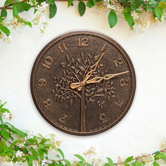 a clock on the side of a building with flowers around it and leaves surrounding it