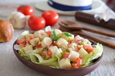 a wooden bowl filled with pasta salad on top of a table next to bread and tomatoes