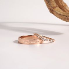 two gold wedding rings sitting on top of a white table next to a piece of wood