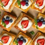 many small desserts with strawberries and blueberries on them are arranged in rows