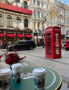 two cups of coffee sitting on top of a table next to a red phone booth