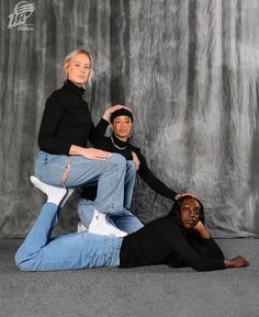 two women sitting on top of each other in front of a gray background, one with her legs crossed