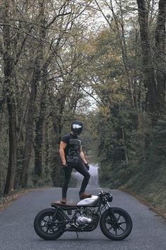 a man riding on the back of a motorcycle down a tree lined road in front of trees