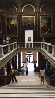 people are walking up and down the stairs in an ornate building with paintings on the walls