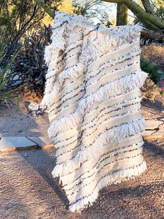 a large piece of cloth hanging from a tree in the middle of a dirt field