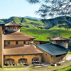 a large building with many windows in the middle of a green field and hills behind it