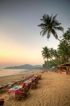 tables and chairs are set up on the beach for an outdoor dining event at sunset