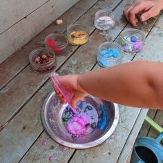 a child's hand is in a bowl filled with colored paint and other paints