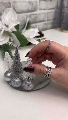 a woman's hand with red nail polish and silver christmas decorations on a white table