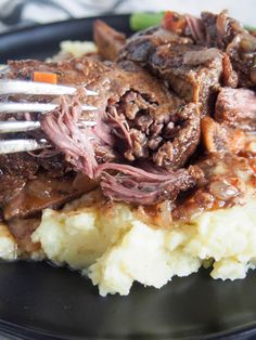 a plate with mashed potatoes, meat and gravy on it next to a fork