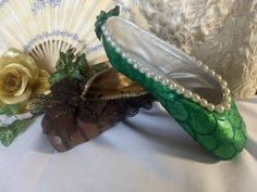 there is a green shoe with pearls on it next to a flower and a fan