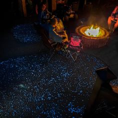 people sitting around a fire pit with blue lights on the ground and one person standing next to it