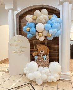 a teddy bear sitting on top of a basket filled with blue, white and gold balloons