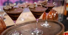 three chocolate martinis sitting on top of a wooden tray next to some wine glasses