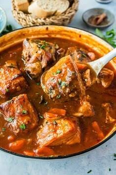 a pot full of stew with meat in it and bread on the table next to it