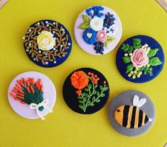 four embroidered buttons with flowers and bees on them sitting on a yellow table cloth covered surface