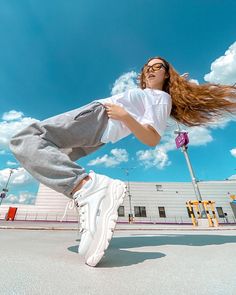 a woman is jumping in the air with her hair flying through the air while wearing white sneakers