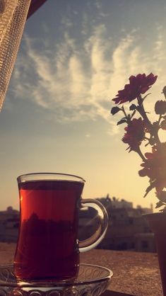 a cup of tea sitting on top of a table next to a vase filled with flowers