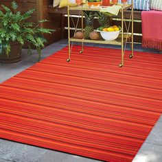 an outdoor area with a red rug, potted plants and fruit on the table