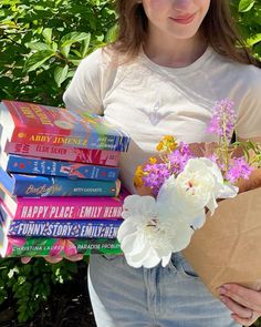 a girl holding a bunch of books and flowers