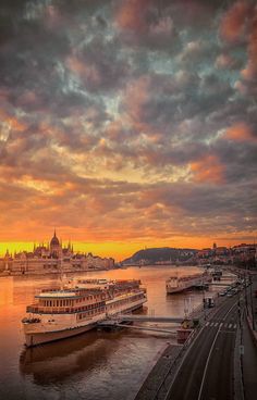 a large boat floating on top of a river next to a city under a cloudy sky