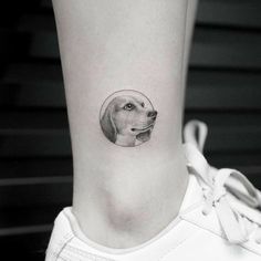 a black and white photo of a dog's head in a circle tattoo on the ankle