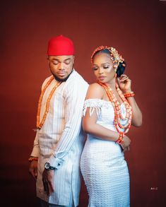 a man and woman standing next to each other in front of a red wall wearing traditional african clothing