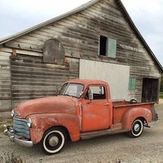 an old red truck parked in front of a barn