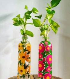 two vases with flowers painted on them sitting on a wooden table next to each other