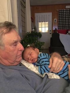 an older man holding a sleeping baby in his lap