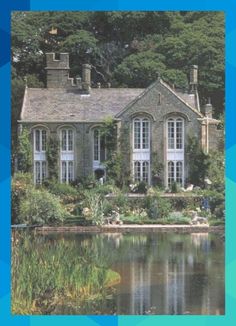 a large house sitting on top of a lush green hillside next to a lake and forest