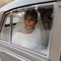 a woman in a white wedding dress sitting in a car with a veil over her head