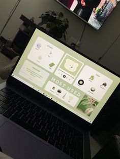 an open laptop computer sitting on top of a desk next to a television monitor and potted plant