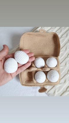 a person holding four white balls in a case on a bed with a knitted blanket