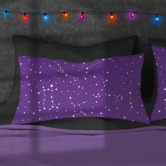 two pillows on a bed with string lights in the background, and one is purple