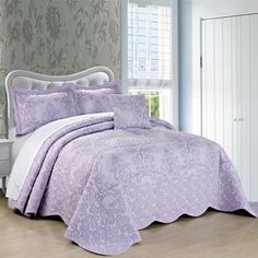 a bed with purple comforter and pillows in a room next to a white dresser