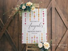 a welcome sign with flowers and greenery hangs on a wooden wall in front of a barn door