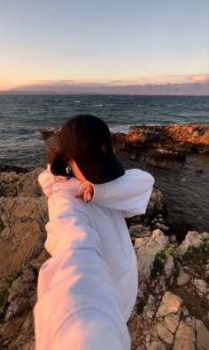 a person sitting on rocks near the ocean with their arms wrapped around each others neck