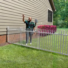 a man standing next to a white fence in front of a house with his hands up