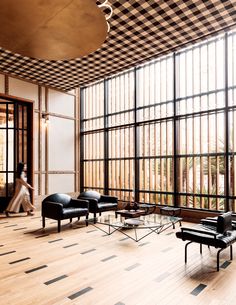 a woman is walking in an empty room with black leather furniture and large glass windows