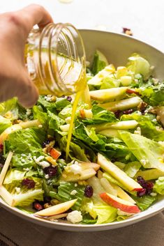 someone pouring dressing onto a salad in a bowl