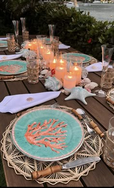 a table set with plates and candles on top of a wooden table next to water