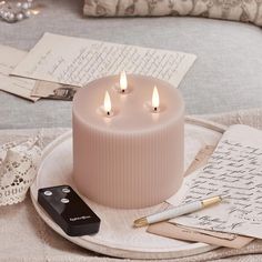 three lit candles sitting on top of a white plate next to an envelope and pen