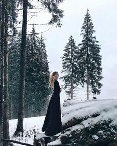 a woman standing in the snow near some trees